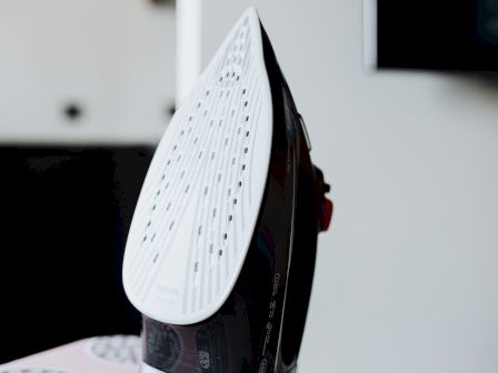 An iron standing upright on a patterned table, with its soleplate facing left and a modern, compact base.