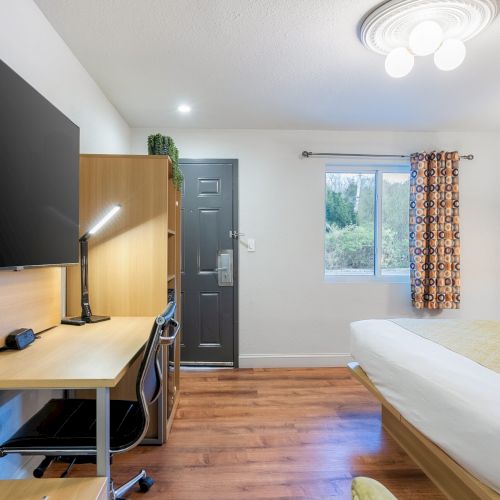 A bright, cozy living room with a wall-mounted TV, sofa, coffee table, and a homey dining corner, featuring warm wood tones and a blue accent wall.